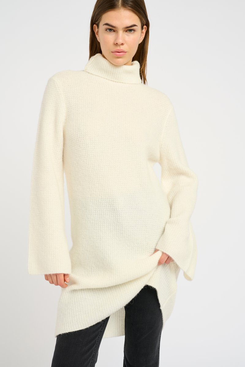 Maglione a collo alto in bianco sporco, con maniche a campana lunghe, motivo testurizzato e spacchi laterali per facilitare i movimenti.