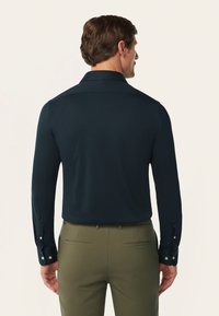 Navy langemouwshirt met een zachte textuur, knoopmanchetten en een klassieke kraag, gecombineerd met olijfgroene broeken met achterzakken.