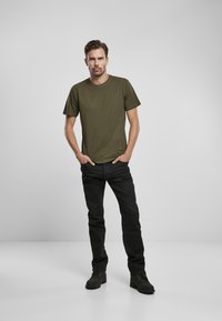 Camiseta de manga corta verde oliva combinada con jeans negros. El corte es holgado, con un cuello redondo y una textura de tela suave.