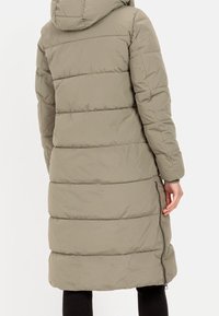 Kurtka puchowa w jasnym khaki z kapturem, z poziomymi pikowanymi panelami, zamkiem błyskawicznym z boku i długością do połowy uda.
