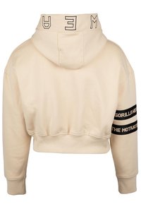 Hoodie corto beige con cappuccio, caratterizzato da testo nero sul colletto e due strisce nere con testo bianco sulla manica. Texture liscia.