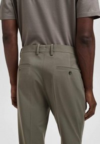 Grijze korte mouw herenoverhemd gecombineerd met olijfgroene op maat gemaakte broeken met een slim fit, achterzakken en knoopdetails.