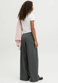 Pelēkas plaša piegriezuma bikses ar teksturētu rakstu, kopā ar baltu T-kreklu un gaiši rozā adītu džemperi, kas pārmests pāri plecam.