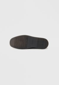 Semelle d'une chaussure habillée noire avec des sections de grip texturé et un logo Calvin Klein au centre, sur un fond clair et uni.