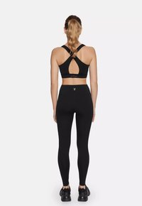 Black sports bra with a cross-back design featuring a cutout, paired with high-waisted black leggings and black athletic shoes.