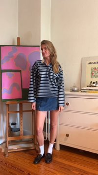 Camisola polo de mangas longas às riscas em azul-marinho e branco, emparelhada com uma saia mini de ganga. Sapatos moccasins pretos e meias brancas até ao tornozelo completam o look.