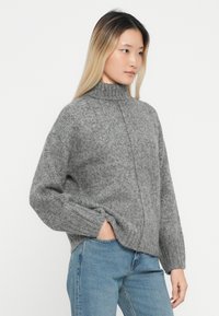 Hallhalli hall sweater kõrgema kaelusega, laiade varrukatega ja lõdva istuvusega. Tekstureeritud kangas ja nähtavad õmblused. Kombineeritud siniste teksadega.