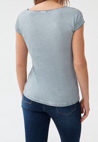 Jasnoniebieski t-shirt z krótkim rękawem i dekoltem w łódkę, miękka w dotyku, z lekko zaokrąglonym dołem, w połączeniu z ciemnoniebieskimi dżinsami.