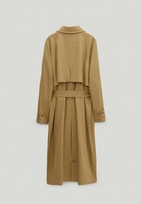 Trench coat beige à double boutonnage, taille ceinturée, col cranté et détails de manches boutonnées. Présente un pli au dos.