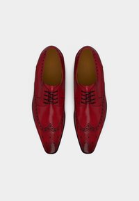 Κόκκινα δερμάτινα παπούτσια για κομψή εμφάνιση, με μυτερή μύτη, διακοσμητικές τρύπες brogue και μαύρα κορδόνια. Ομαλή υφή με γυαλιστερό φινίρισμα.