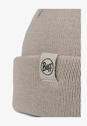 Helle beige gestrickte Mütze mit umgeschlagenem Saum, ausgestattet mit einem weißen Stoffetikett mit schwarzem "Buff"-Logo. Strukturmaterial mit geripptem Muster.