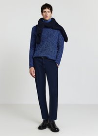 Blauer Pullover mit Struktur, marineblaue Hose und schwarze Stiefel. Ein marineblauer Schal liegt locker über den Schultern und erzeugt einen geschichteten Look.