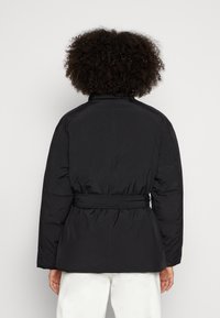 Casaco puffer preto com cinto, apresentando uma gola alta e uma textura suave. Inclui seções franzidas na cintura e nas costas.