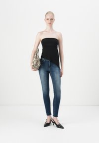Black strapless top, blue skinny jeans, and black heeled mules. Model holds a snakeskin-patterned handbag, standing against a white backdrop.