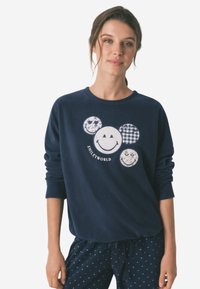 Marineblå sweatshirt med fire cirkulære smiley-ansigt designs i forskellige mønstre og farver, med teksten "SMILEY WORLD" nedenfor. Blød tekstur.