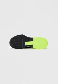 Black athletic shoe sole with zigzag tread pattern, featuring a bright green section at the heel and a textured surface for grip.