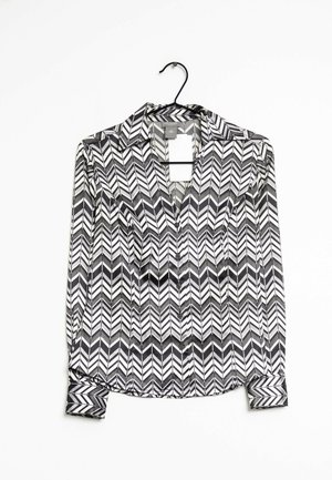 Camicia a maniche lunghe bianca e nera con motivo a zigzag; presenta un colletto, una chiusura con bottoni e polsini abbottonati; realizzata in un tessuto morbido.