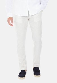 Pantaloni beige a righe leggeri con taglio slim, caratterizzati da una sottile texture, tasche laterali e abbinati a scarpe scamosciate scure da infilare.