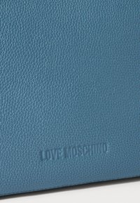Textura de pele azul com pedrinhas com o logótipo em relevo "LOVE MOSCHINO" no canto inferior direito.