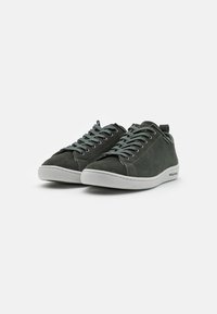 Grüne Wildleder-Sneaker mit weißen Gummisohlen, runder Zehenpartie und fester Schnürung. Verfügt über dezente Nähte und eine Schlaufe zum Anziehen im Fersenbereich.