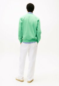 Sweatshirt vert menthe avec des accents côtelés au col et aux poignets. Associé à un pantalon blanc et des chaussures de couleur claire. Design simple et décontracté.