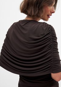 Brown ruched top with soft fabric, featuring gathered texture along the shoulders and sleeves, creating a flowing silhouette.