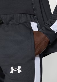 Fekete sportos joggerek fehér oldalsávokkal, húzózsinórral a deréknál, és bal alsó részen fehér Under Armour logóval.