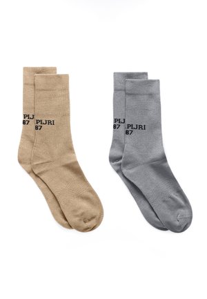 Dwie pary skarpetek sięgających do połowy łydki, jedna beżowa, a druga szara, każda z napisem "PIJRI 87" wydrukowanym czarnym tekstem w pobliżu góry.