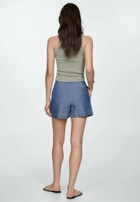 Pantalones cortos de mezclilla con un corte relajado, color azul, dobladillo sin acabar y detalles de costura sutiles. Combinados con una camiseta de tirantes ajustada de color verde oliva.