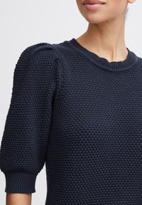 Dunkelblaues Strickpullover mit einem strukturierten Waffelmuster, rundem Ausschnitt und puffierten kurzen Ärmeln. Rippbündchen.