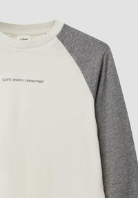 Raglan-Sweatshirt mit crèmefarbenem Körper und grauen Ärmeln. Mit dem Text "SLVR STUDIOS | DEPARTMENT" auf der Vorderseite. Weicher Stoff mit lockerer Passform.