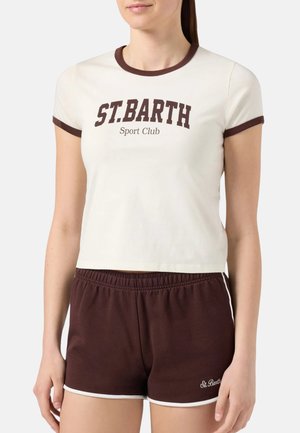Donna con t-shirt corta color crema con la scritta "ST. BARTH Sport Club" e pantaloncini marroni con bordino bianco e logo "St. Barth".