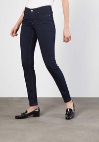 Tynne jeans laget av mørk denim med fremtredende sømmer og en tettsittende design. Kombinert med svarte hæl loafers, som viser en polert look.