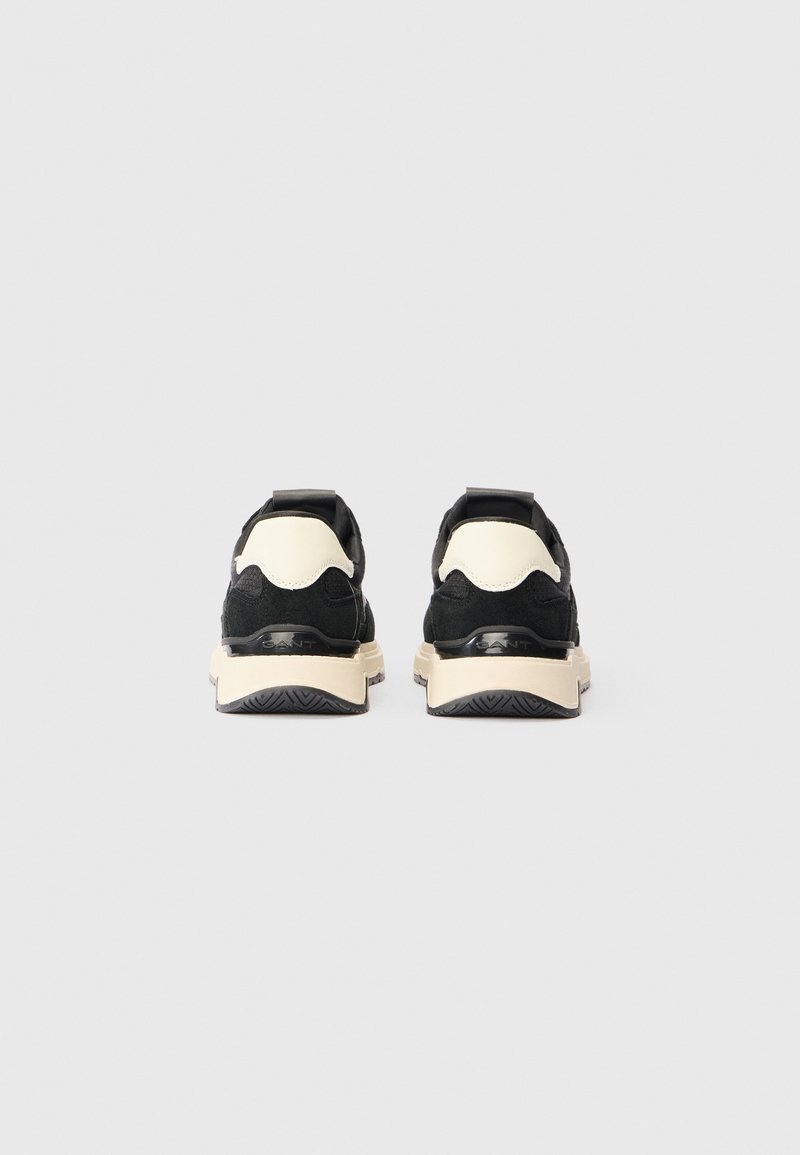 Czarno-kremowe sneakersy z teksturowaną cholewką, wyściełanym kołnierzem i grubą białą podeszwą z bieżnikiem. Logo widoczne z tyłu.
