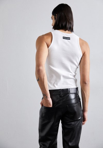Λευκό ριγέ αμάνικο μπλουζάκι με μαύρη ετικέτα μάρκας, συνδυασμένο με ψηλόμεσα μαύρα δερμάτινα παντελόνια που διαθέτουν πλαϊνές τσέπες και διακριτική υφή.