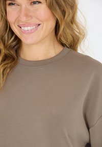 Bruine ronde hals sweatshirt van zacht materiaal met een minimale textuur, met een relaxte pasvorm en subtiele stikdetails bij de kraag.