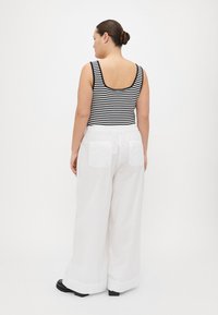 Svart og hvit stripet tank topp med scoop bak, kombinert med løse hvite vidde bukser med to baklommer. Svarte sko.