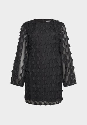 Tunique noire à manches longues et transparentes, ornée de détails en tissu ondulés en relief, sur un fond uni.