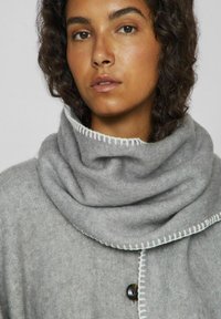 Bufanda de mezcla de lana gris con un diseño plegado, que presenta acentos blancos cosidos a lo largo de los bordes y un cierre de botón en una prenda texturizada gris.