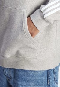 Grå sweatshirt med en framficka, ribbade muddar och tre vita ränder på ärmen. Bärs med blå denimjeans.