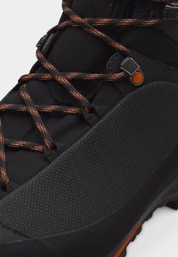 Μαύρο ορειβατικό μποτάκι με υφασμένο κάλυμμα στα δάχτυλα και μαύρα κορδόνια με πορτοκαλί και λευκές λεπτομέρειες.