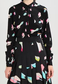 Blusa negra con formas abstractas y coloridas en rosa, azul claro y amarillo; de mangas largas, con botones en la parte delantera y de tela suave. Falda plisada con un patrón similar.