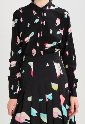 Blusa nera con forme colorate astratte in rosa, azzurro e giallo; maniche lunghe, frontale con bottoni e tessuto morbido. Gonna plissettata con un motivo simile.