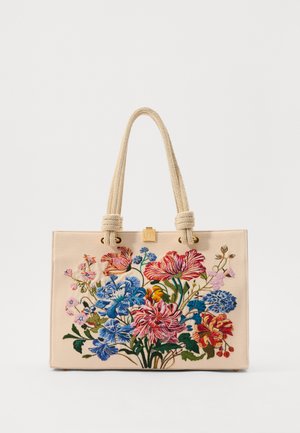 Beige canvas tote bag med farverig blomsterbroderi i rød, blå og pink; rebhåndtag og en guldtonet logo-accents.