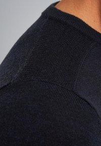 Námořnická modrá pletená svetr s blízkým záběrem, zobrazující strukturovaný povrch s hladkými a ribbed oblastmi, s kulatým výstřihem a detailem švu na rameni.