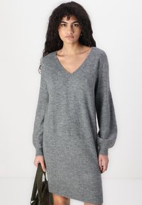 Robe pull en tricot grise avec un col en V, de longues manches bouffantes et un ourlet côtelé. Texture douce, longueur genou et coupe décontractée.