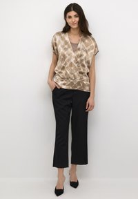 Blusa beige con motivo astratto, maniche corte, vita aderente; abbinata a pantaloni neri cropped e décolleté nere a punta.