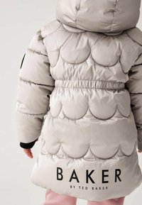 Pufferjakke i lysegrå med bølget mønster, snøre i taljen, og logoet "BAKER by TED BAKER" bagpå. Blødt, skinnende materiale.