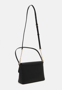 Sac à bandoulière en cuir noir avec sangle réglable, accents en chaîne dorée et rabat lisse et courbé sur fond blanc.