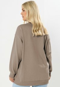 Sudadera taupe de gran tamaño con mangas largas, puños y dobladillo acanalados. Tejido suave, corte relajado, diseño minimalista, combinado con jeans azul claros.